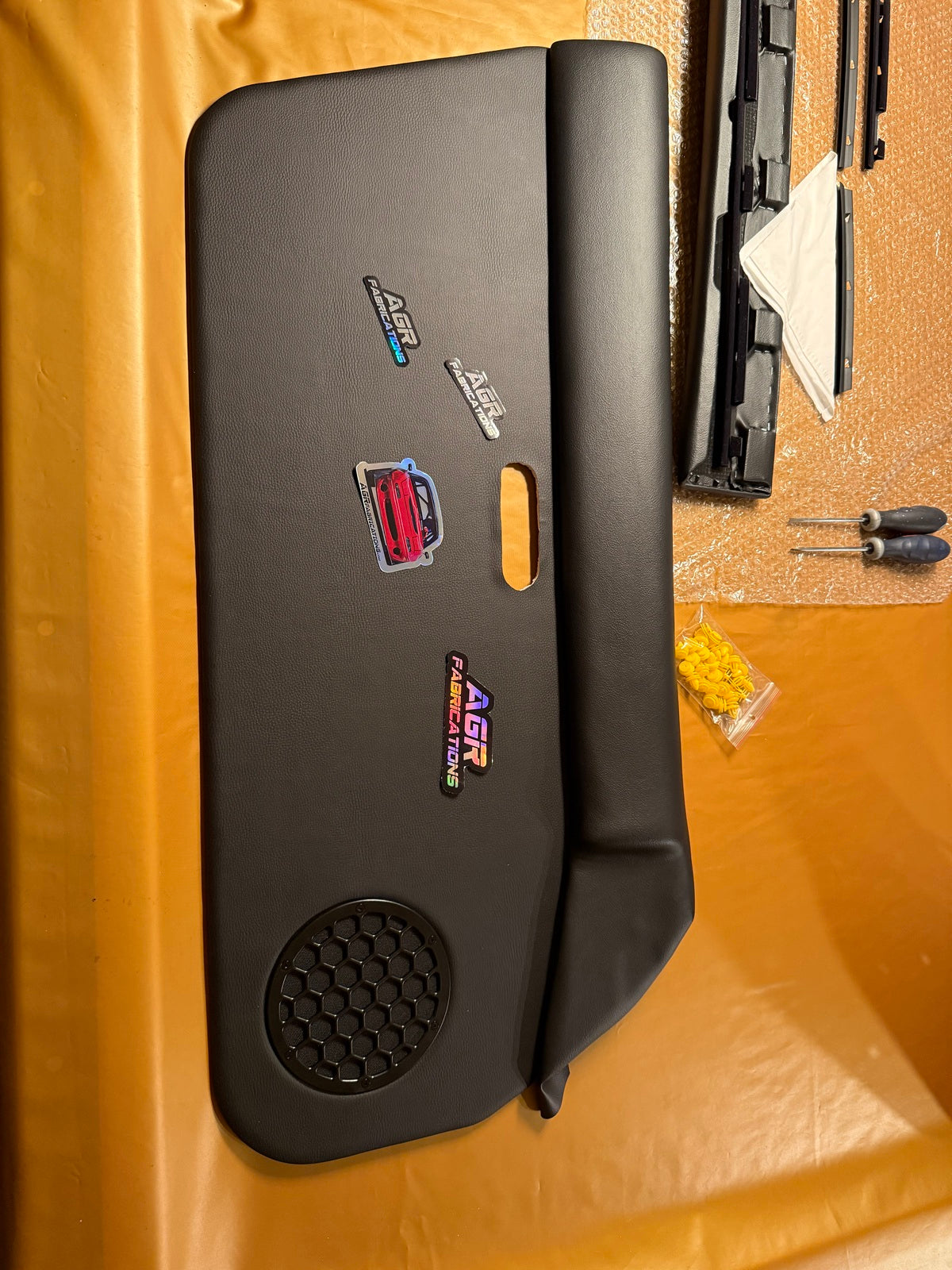 A black textured leather car interior trim panel with a circular honeycomb grille cutout, shown on orange background.