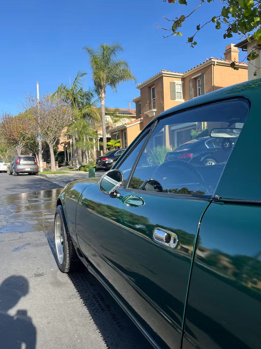 Green miata parked on a street with palm trees and buildings in the background