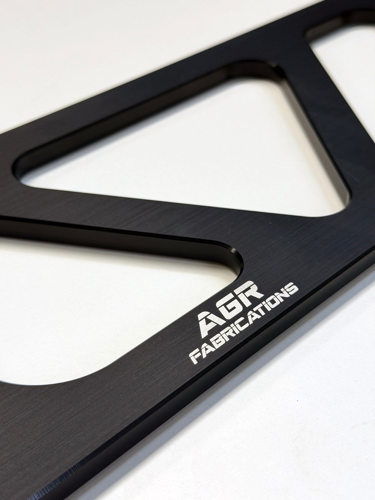 Close-up of a black metal brace  with cutouts and white engraved text reading 'AGR FABRICATIONS' on a white background.